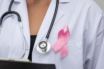 Closeup of a physician's whitecoat with a pink breast cancer–awareness ribbon pinned next to her stethescope