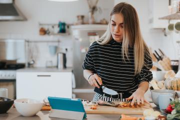A young woman is preparing food while watching a cooking class on a tablet