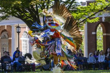 An adult in a traditional Native American outfit dances.