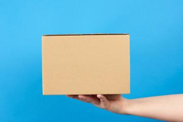 Hand holds a brown cardboard box of paper on a blue background