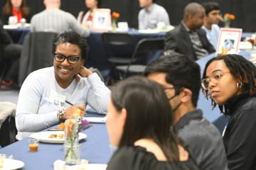 A adult smiles at others sitting around the dinner table.