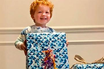 A young boy smiles while holding a gift wrapped in blue wrapping paper.