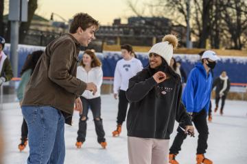 Two students smile at each other as they skate on a crowded ice rink.