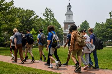 Students walk on a brick path on the Johns Hopkins University campus. Gilman Hall is in the background.
