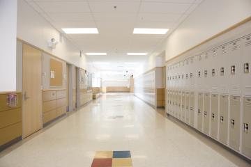 An empty school hallway, with lockers on one wall and doors to classroom on the other