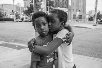 Black and white photo of two children hugging on a street corner in Baltimore