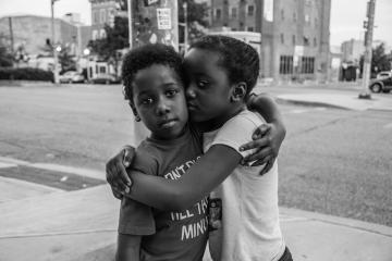Two siblings hug each other on a Baltimore street corner