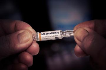 A closeup of two hands holding a small vial labeled Methadone
