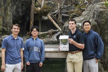 Students from the Johns Hopkins Multidisciplinary Engineering Design course showcase their bobcat feeding system in front of the bobcat enclosure at the Maryland Zoo