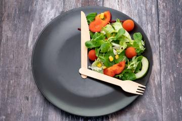Salad arranged on a black plate with a fork and knife arranged like hands on a clock