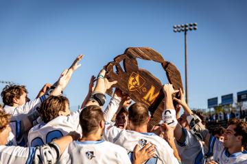 Johns Hopkins lacrosse players hold up a large wood crab trophy
