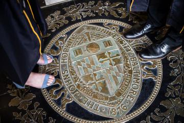 Two sets of feet take their first steps onto the JHU seal in Gilman Hall