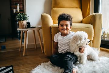 Smiling young child and a curly-haired dog sit on the floor at home