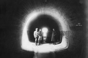 Three men stand in an underground tunnel in 1907. A note written on the image reads 