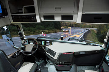 Rendering of the interior of an autonomous vehicle. No one is seated at the steering wheel, but the car's computer system has identified another car on the road.