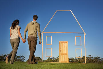 Man and woman walk toward a wood-framed outline of a house