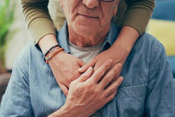 A woman's hands rest on the shoulders of an elderly loved one