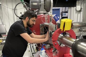 An engineer in a black shirt works on a large red machine.