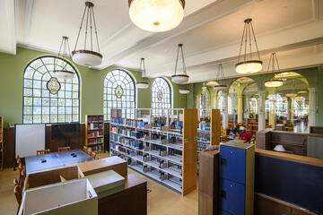 A green room with stained glass windows, hanging lights, and desks where students are studying