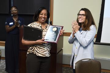 Marie Wilson receives a plaque for her 50 years of service to Johns Hopkins University. Two of her coworkers applaud her.