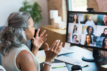 Manager at a desk talks to employees who appear on her monitor.