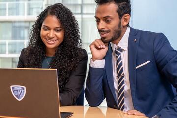 Two adults in suits smile while looking at the screen of a laptop with the Johns Hopkins logo on it.