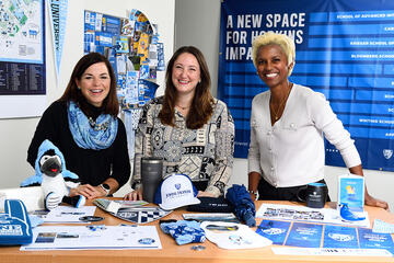 Abby Jackson, Beth Fritzinger, and Marina Cooper with an array of JHU-branded materials and merchandise.