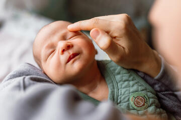 An adult hand touches the eyebrow of a newborn