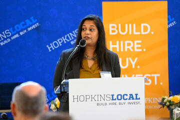 A woman speaks at a podium with a HopkinsLocal sign