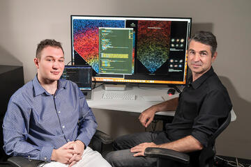 Photo of Nikita Shtarkman and Brice Menard sitting in front of a large computer monitor