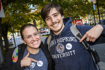 Two smiling college students wearing Johns Hopkins University merch point to the 