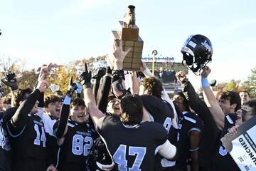 Football players in black jerseys with blue numbers hoist a trophy and celebrate