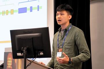 Kuan-Hao Chao stands at a podium and speaks. There is a desktop screen on the podium.