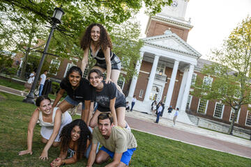 Six students get on their hands and knees to make a pyramid in front of Gilman Hall.