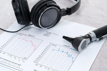 Photo of hearing test equipment, including a chart, headphones, and an otoscope 