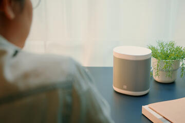 A man sitting at a desk uses a smart speaker