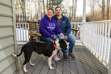 Joel Searfoss and Erica Klinedinst sitting on a porch swing with Emma, a recent rescue, standing at their feet. 