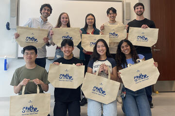 Student volunteer with SOOTHE hold up canvas tote bags in a group photo