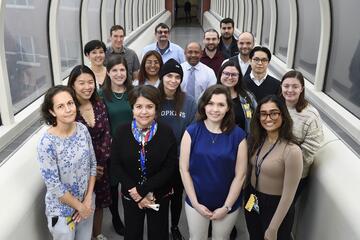 18 people smile for a group picture while standing in a glass walkway.