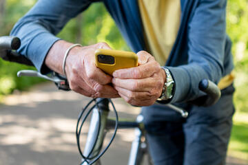 Man leaning on bicycle handlebars using an app on his mobile phone.