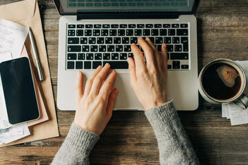 Overhead view of a woman's hands typing on a laptop