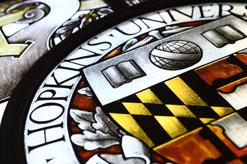 Colorful stained glass window from Hutzler Reading Room showing Hopkins shield