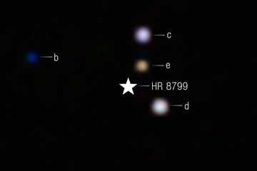 Blurry planets of the HR 8799 system against a black background, captured in infrared with Webb’s NIRCam. A star symbol marks the blocked-out host star