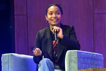 Yara Shahidi sits on a chair while speaking into a microphone.