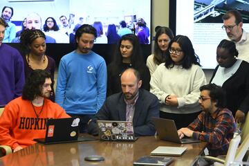 A large group of people look at a laptop screen.