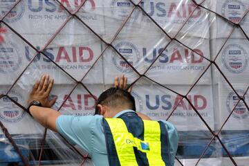 An individual pushes against a large cargo of USAID boxes