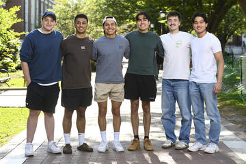 A group of six college students smile for the camera with their arms around each other.