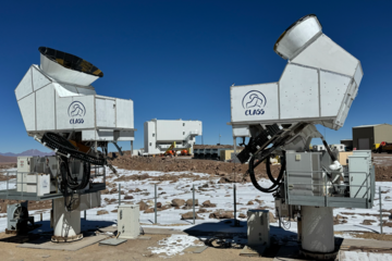 Two telescopes set up on the ground with patches of snow surrounding them, blue sky in the background