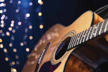 An acoustic guitar on a dark blue background with white twinkle lights