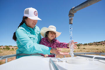 A young Diné (Navajo) girl assists her aunt in collecting water for their livestock